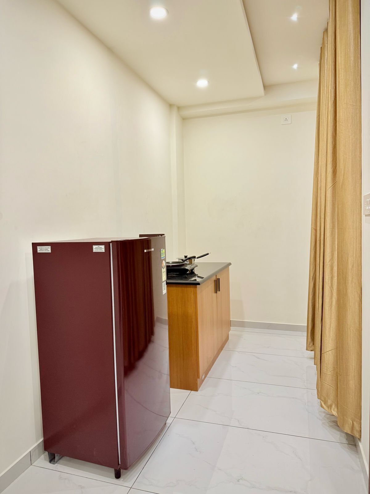 A compact kitchen with a refrigerator, a wooden counter, and a curtain.