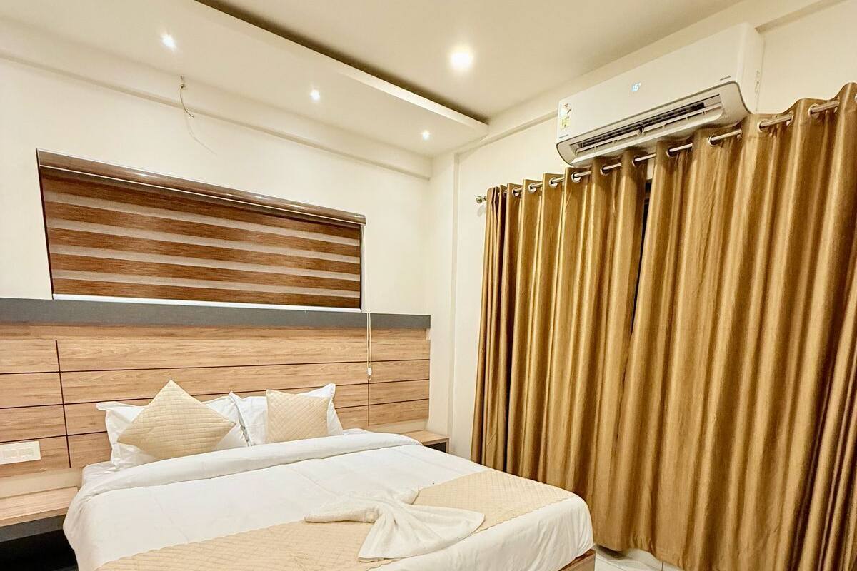 A modern hotel room with a large bed, wooden headboard, and a built-in air conditioning unit.