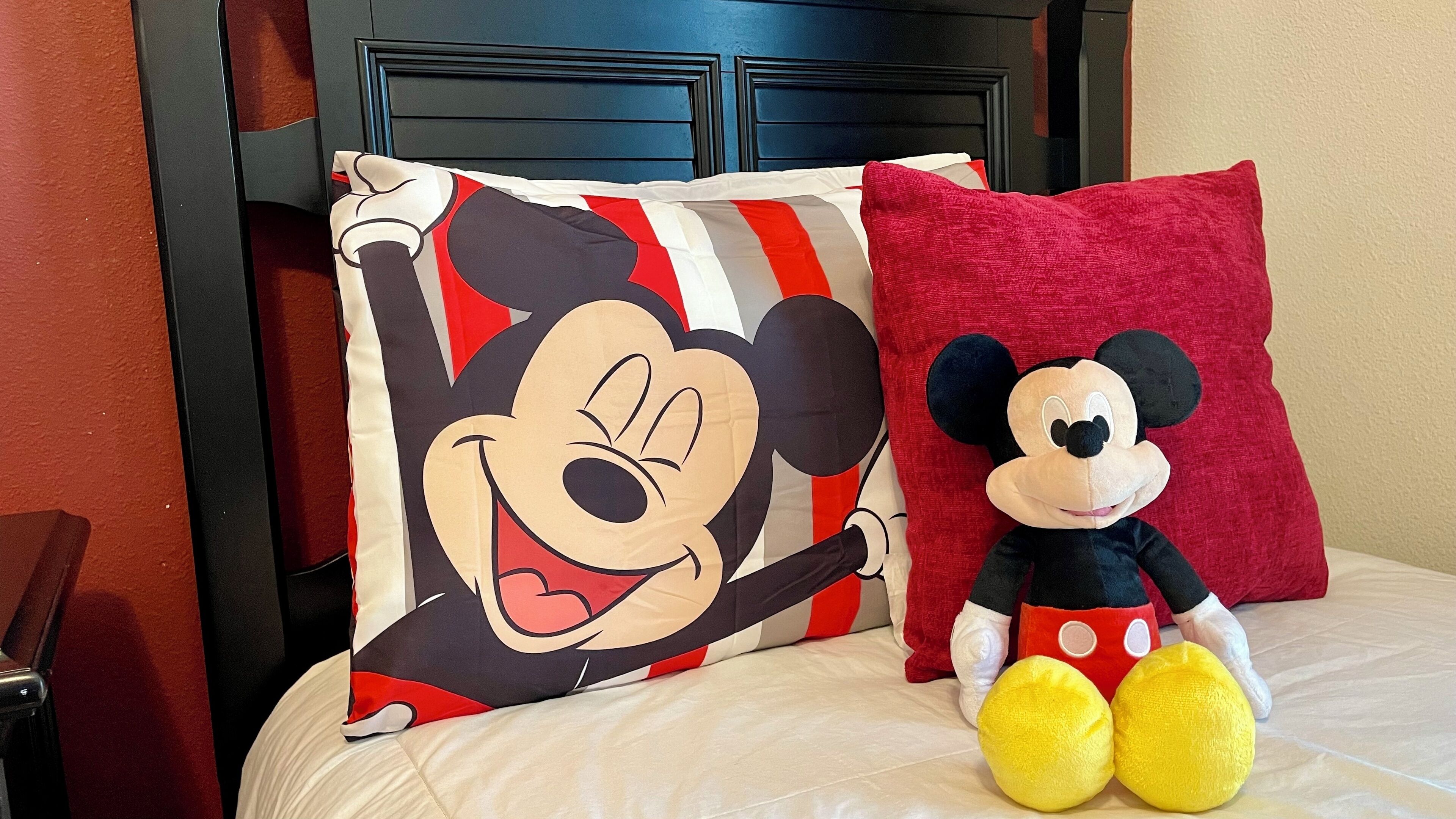 A bed with a Mickey Mouse pillow and a plush toy.