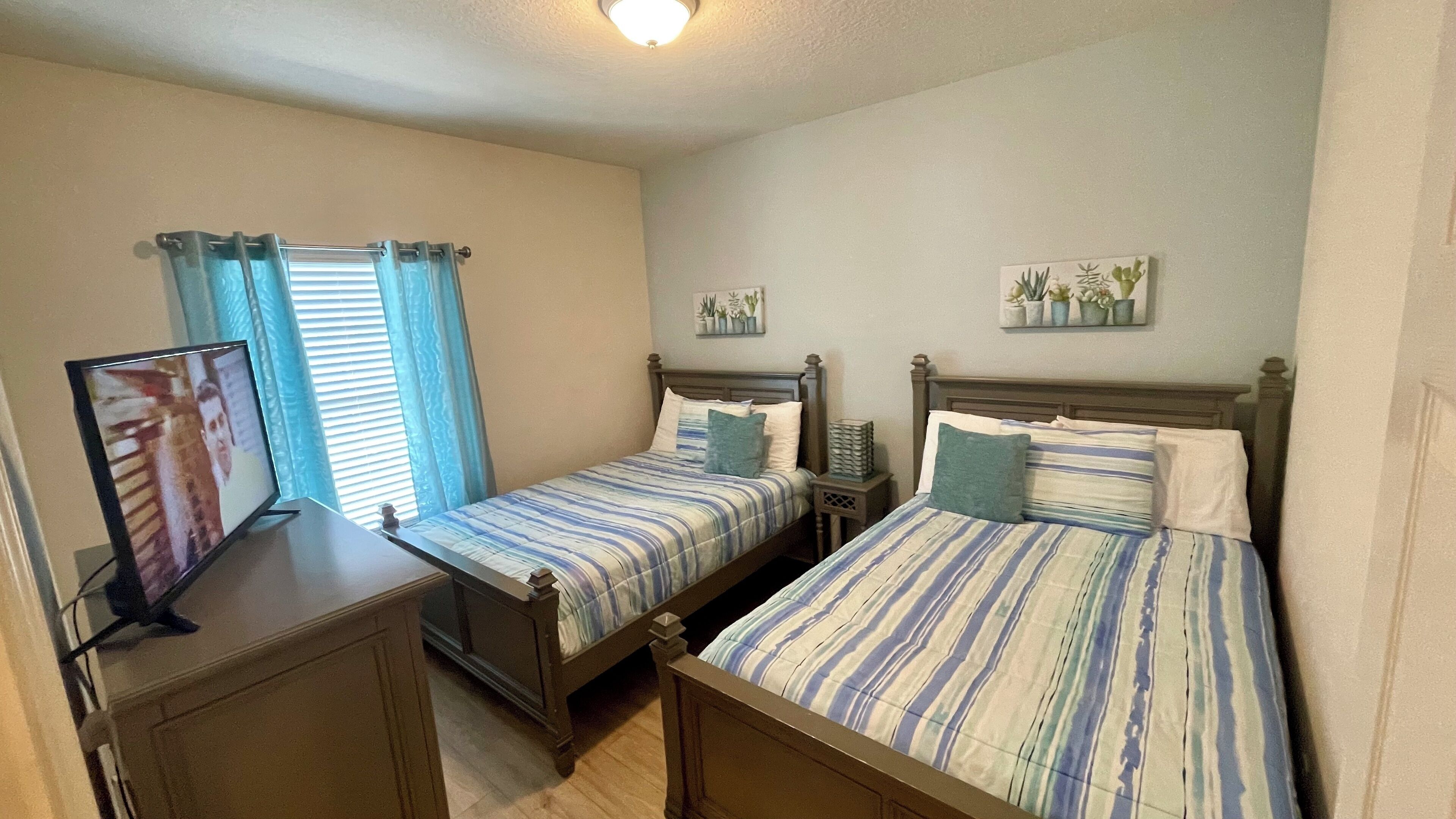 A bedroom with two single beds, a bedside table, a TV, and a window with curtains.