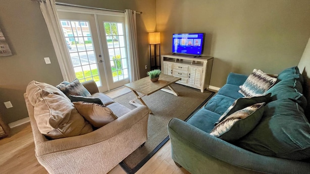 A living room with a sofa, a coffee table, a TV, and a cabinet. - Nice 4bd townhouse near Disney (Kissimmee)