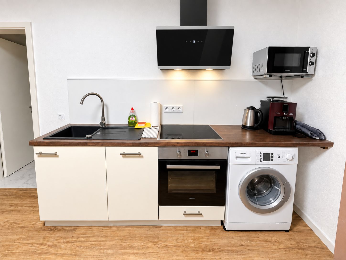 A compact kitchen with a sink, microwave, oven, and washing machine.
