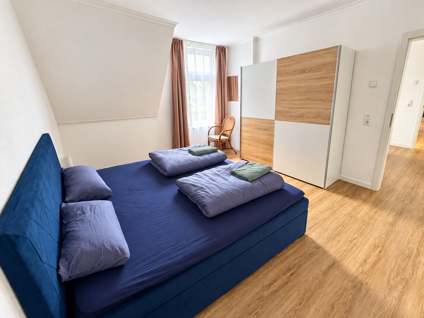 Quarto moderno com uma cama grande, um guarda-roupa de madeira e uma cadeira.