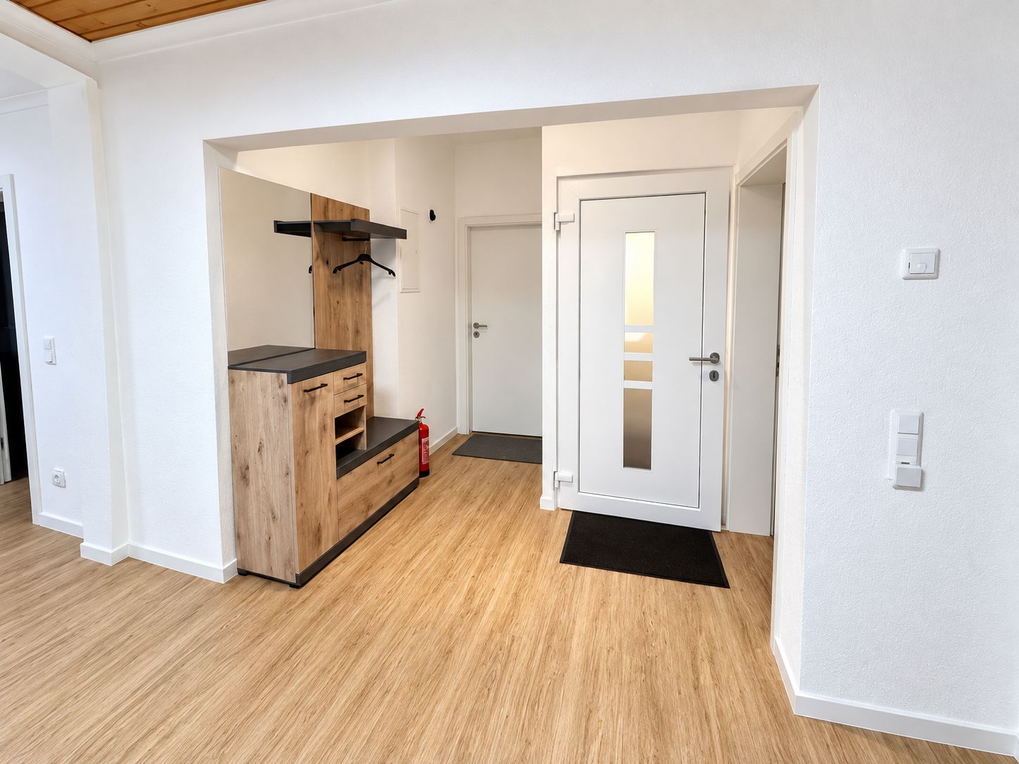 Ein Flur mit einem Holzkasten, einer Tür mit satinierten Glasfeldern und einem Feuerlöscher auf dem Boden.