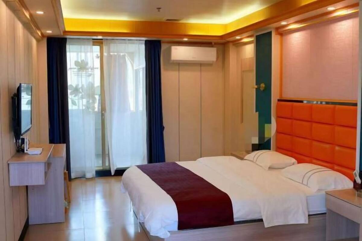 A hotel room with a bed, a desk, a TV, an air conditioning unit, and a sliding glass door.