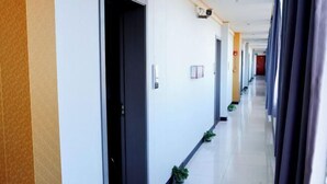 Ένας διάδρομος ξενοδοχείου με πόρτες, γλάστρες με φυτά και μια κάμερα ασφαλείας.
