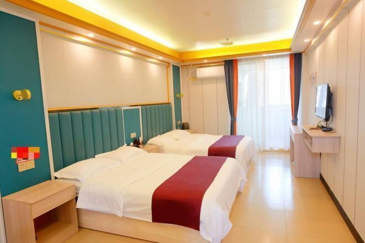 A hotel room with two beds, a TV, a desk, and a window with curtains.