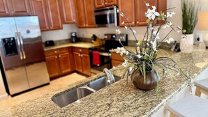 A kitchen with granite countertops, wooden cabinets, stainless steel appliances, and a vase with flowers on the counter. - Spacious 7-bedroom house in Champions Gate (Four Corners)