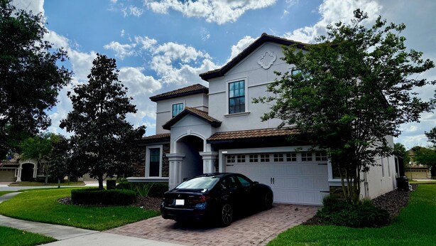 A two-story house with a garage, driveway, and a black car parked in front. - Spacious 7-bedroom house in Champions Gate (Four Corners)