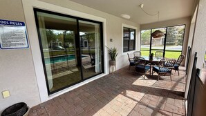 A covered patio area with a pool, a table with chairs, and a sign listing pool rules. - Spacious 7-bedroom house in Champions Gate (Four Corners)