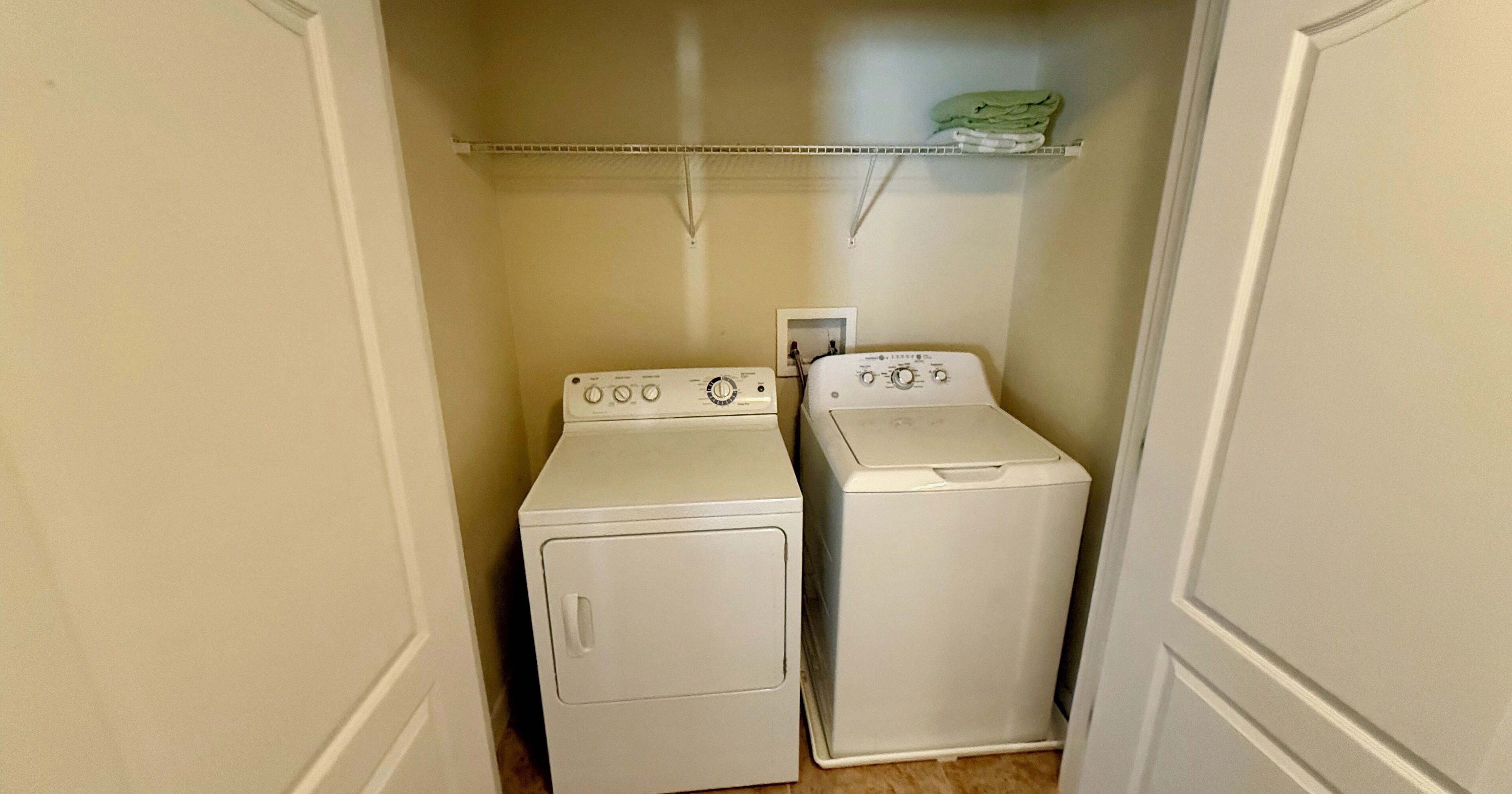 A laundry room with two white washing machines and a shelf above them.