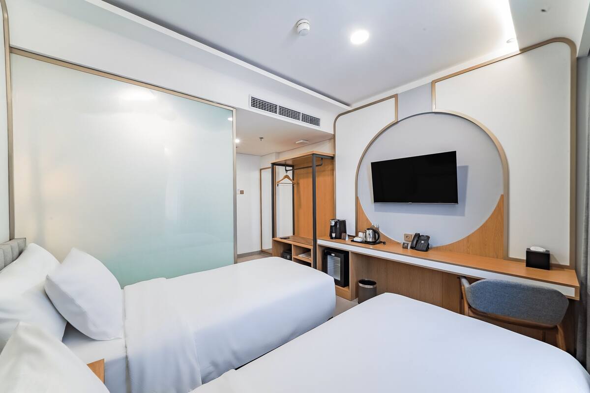 Una habitación de hotel moderna con dos camas, un escritorio con televisor y un pequeño rincón de descanso.