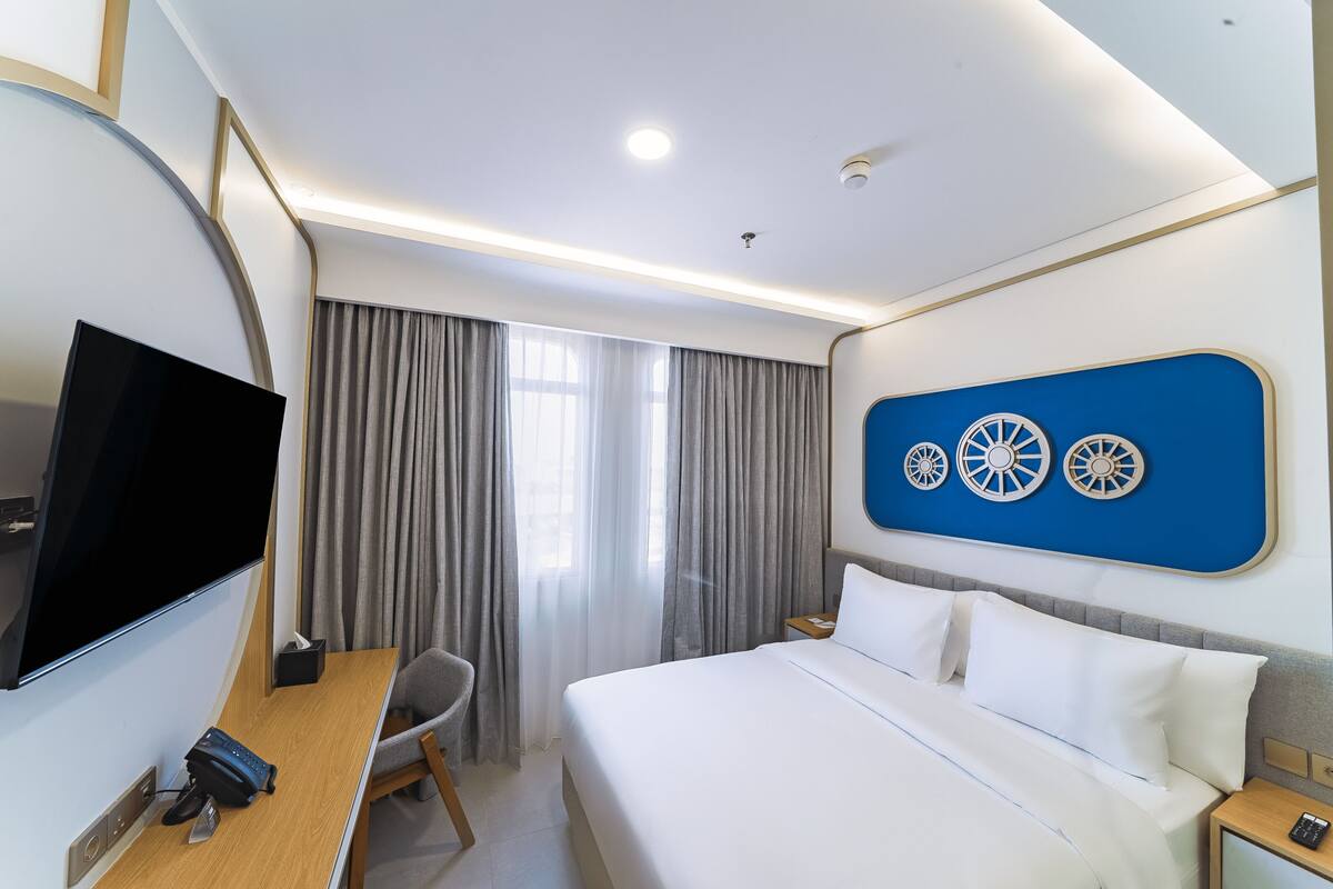 Habitación de hotel con cama, escritorio con computadora, televisor y pared decorada.