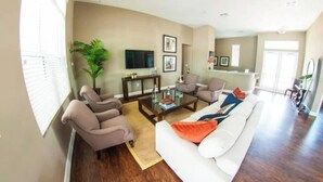 A spacious living room with a white sofa, two armchairs, a coffee table, and a television. - Cozy 3bd home 15 min from Disney (Kissimmee)