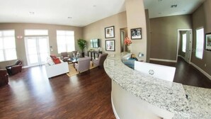A spacious living area with a curved granite counter, a seating area with sofas and armchairs, and a large window providing natural light. - Cozy 3bd home 15 min from Disney (Kissimmee)