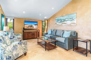 A living room with a sofa, a coffee table, a TV, and a painting on the wall.
