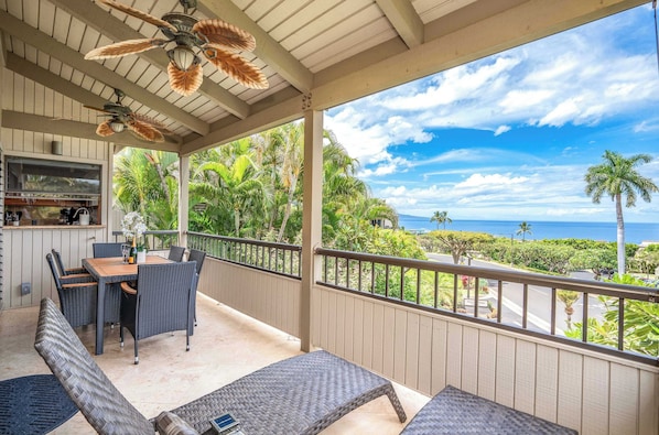 A covered outdoor area with a dining table and chairs, a bar, and a view of the ocean.