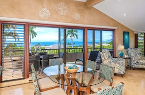 A spacious living area with a glass table, wicker chairs, and a view of the ocean.