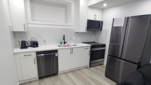 A modern kitchen with white cabinets, a microwave, a stainless steel refrigerator, a dishwasher, and a stove. - Carrington Cozy Suite, Calgary (Calgary)