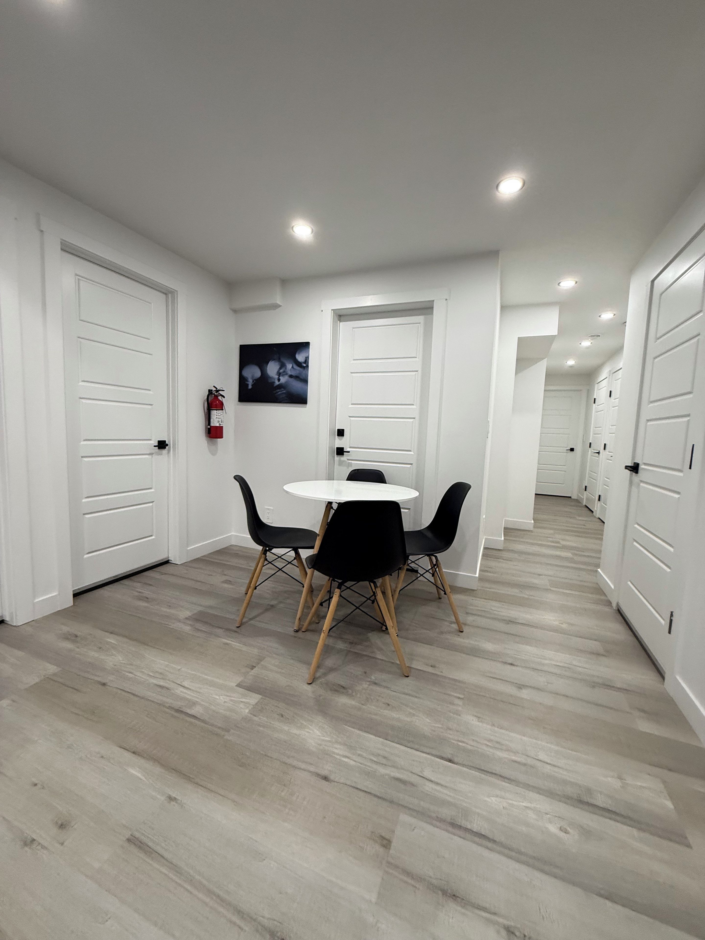 A hallway with white doors, a round table with chairs, and a fire extinguisher mounted on the wall.