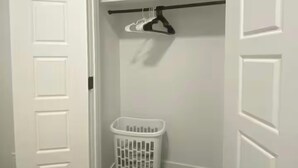 A white closet with a hanging rod and a laundry basket. - Carrington Cozy Suite, Calgary (Calgary)