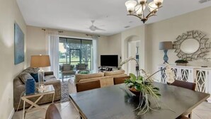 A modern living room with a dark wooden dining table, a sofa, and a TV. - Resort Champions Gate 2 Bd/2Bh - Golf view (Davenport)