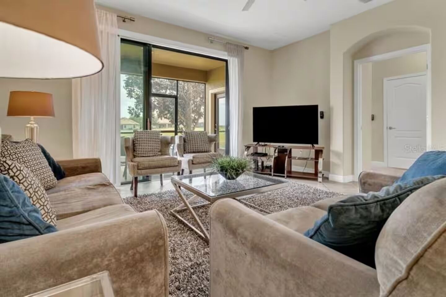 Una sala de estar con un sofá, una mesa de centro, un televisor de pantalla plana y un puerta corrediza de vidrio que da a un balcón.