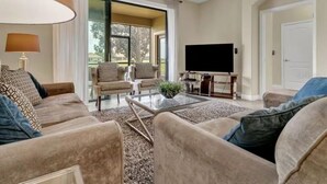 A living room with a sofa set, a coffee table, a flat-screen TV, and a sliding glass door leading to a balcony. - Resort Champions Gate 2 Bd/2Bh - Golf view (Davenport)