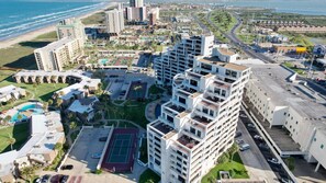A high-rise hotel with multiple floors, a tennis court, and a pool.