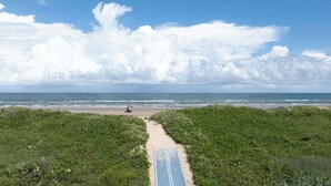 Ein Strandweg führt zum Meer, bewölkter, klarer Himmel.