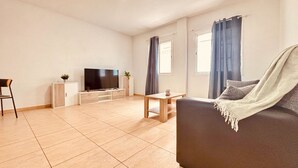 Una sala moderna con un televisor de pantalla plana, un sofá, una mesa de centro y una mesa de comedor.