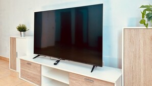 Televisor de pantalla plana sobre un mueble blanco con una planta al lado.