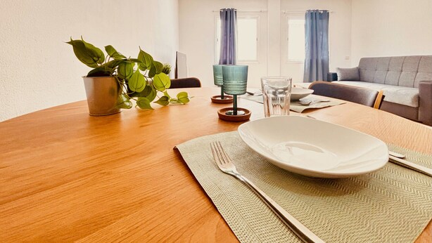Una mesa de comedor con un plato, un tenedor y una servilleta, una planta en maceta y un sofá en una sala de estar.