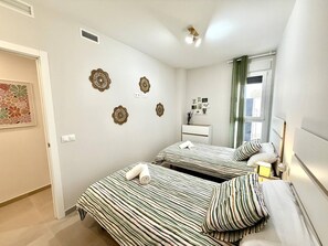 A bedroom with two beds, a small bedside table, a nightstand, a window with curtains, and wall decor. - El rincon de candor by staycare (Rota)