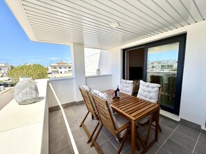 A balcony with a wooden table and chairs, a potted plant, and a view of the cityscape. - El rincon de candor by staycare (Rota)
