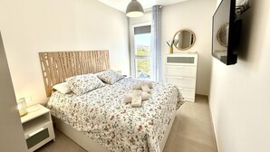 Une chambre à coucher comprenant un lit, une table de chevet, une commode, un miroir et une fenêtre avec des rideaux.