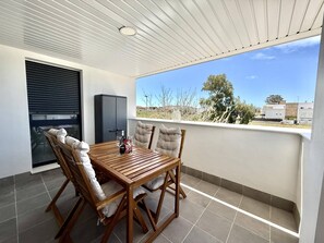 A balcony with a wooden table and chairs, a black cabinet, and a view of the surrounding area. - El rincon de candor by staycare (Rota)