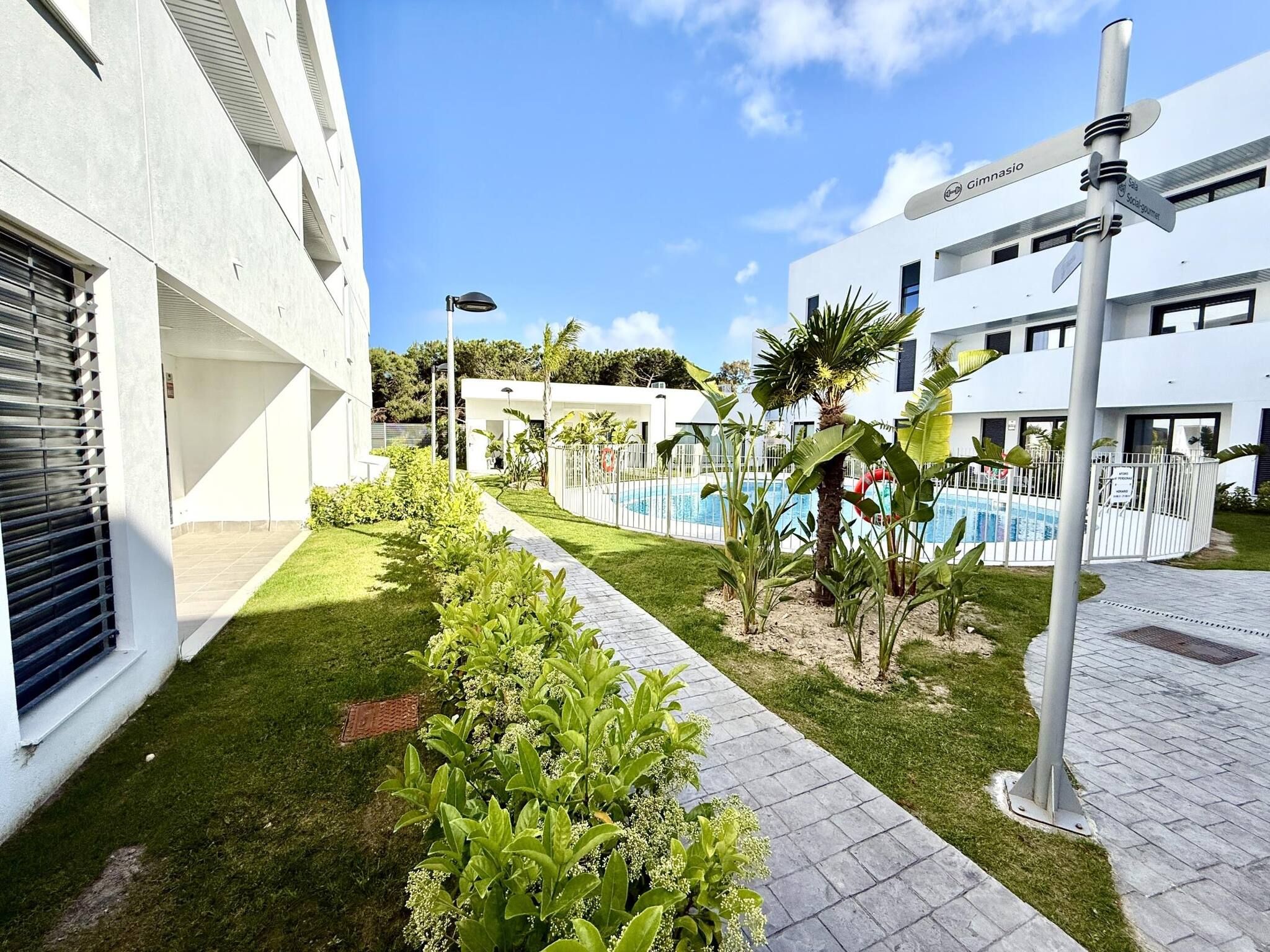 Un edificio moderno con piscina, rodeado de vegetación cuidada y un cielo despejado.