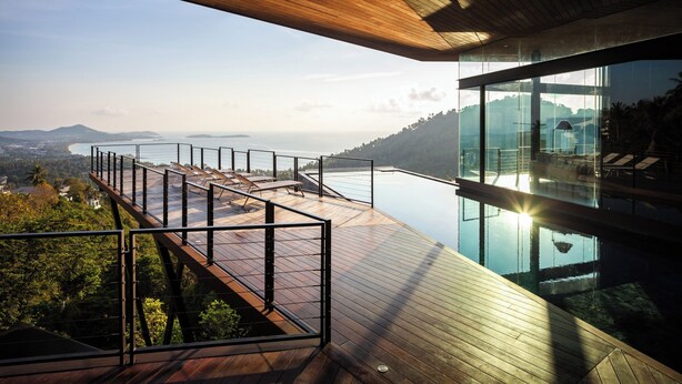 A modern outdoor deck with a glass balustrade overlooking a body of water and distant landscape. - Kelapa House (Koh Samui)