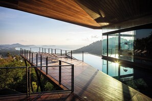 A modern outdoor deck with a glass balustrade overlooking a body of water and distant landscape. - Kelapa House (Koh Samui)