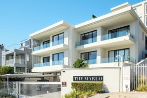 A multi-story building named "THE MARLO" with balconies, a gated entrance, and a clear sky.