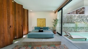 A modern bedroom with a large bed, a view of a pool, and a stone wall. - Modern 2BR Villa Rooftop & Pool (Kuta Utara)
