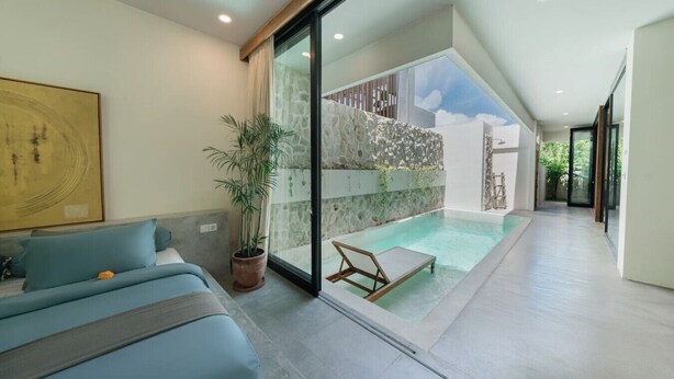 A modern living room with a sofa, a potted plant, and a view of an outdoor swimming pool. - Modern 2BR Villa Rooftop & Pool (Kuta Utara)