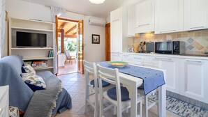 Een knus woongedeelte met een bank, televisie, eettafel, stoelen en een keuken met kasten en apparatuur.