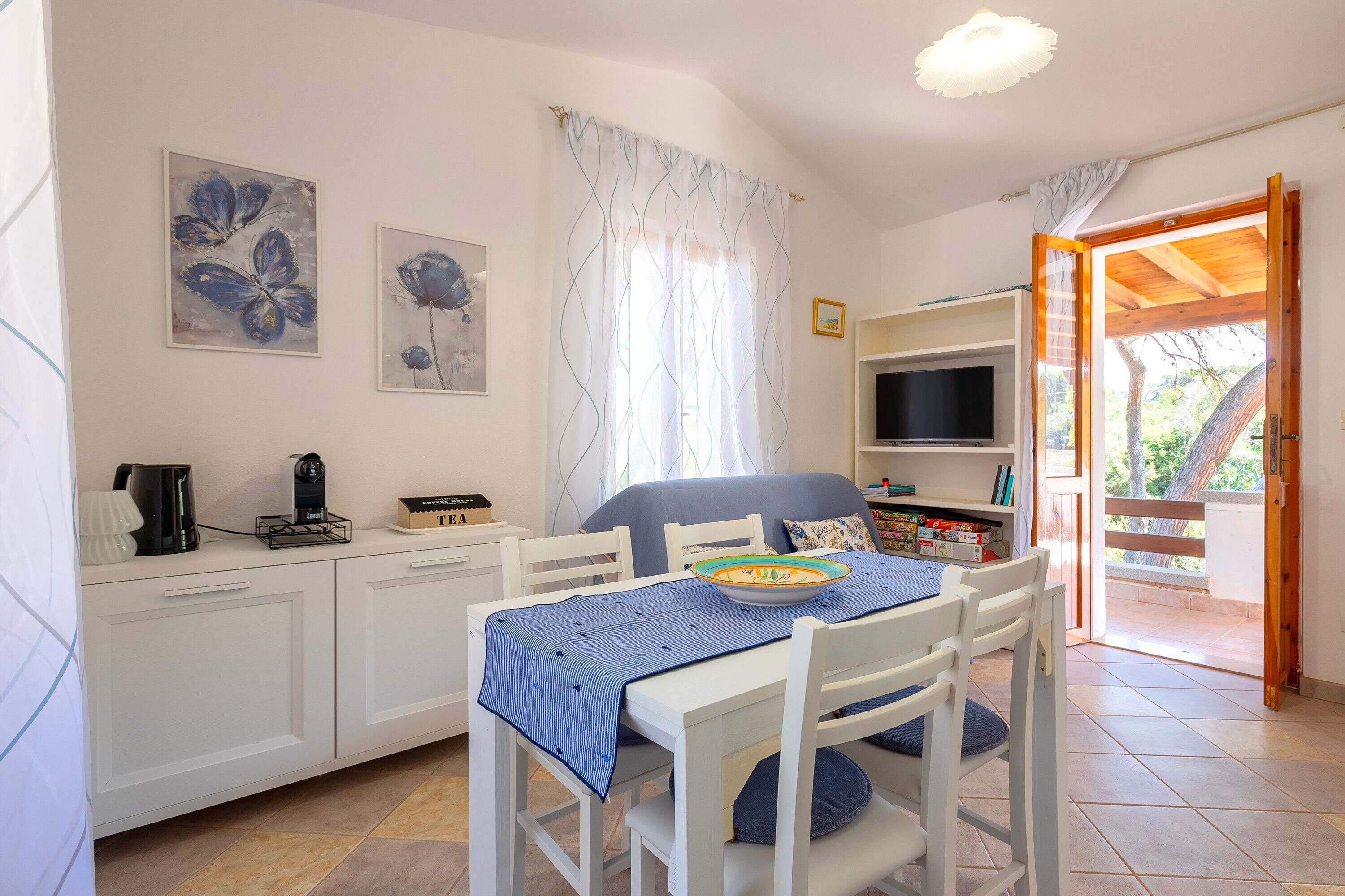A room with a dining table, chairs, a TV, a bookshelf, and a window with curtains.