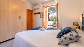 Een slaapkamer met een bed, een kledingkast, een open slaande deur naar een balkon, en een tafel met stoelen buiten.