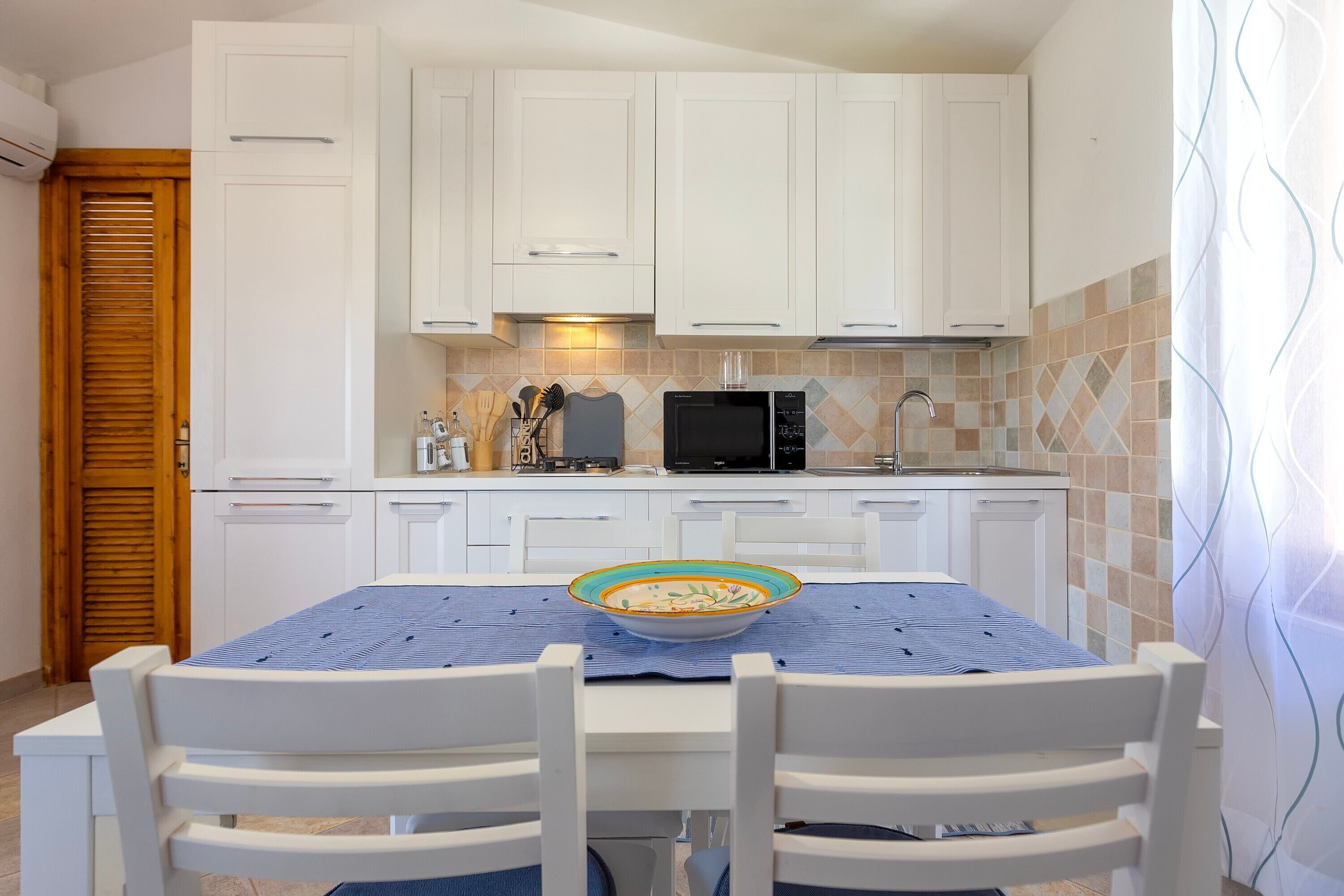 Una cocina con armarios blancos, un microondas y una mesa de comedor con sillas.