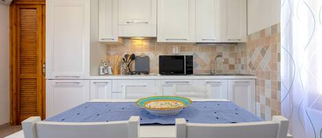 Una cocina con armarios blancos, un microondas y una mesa de comedor con sillas.