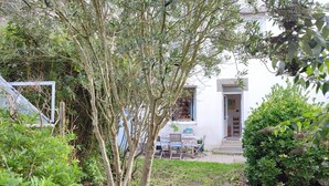 Un jardín con un edificio blanco, una mesa con sillas y una puerta pequeña.