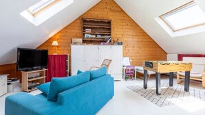 Una habitación estilo loft con televisión, sofá, mesa de madera y cama en altillo.